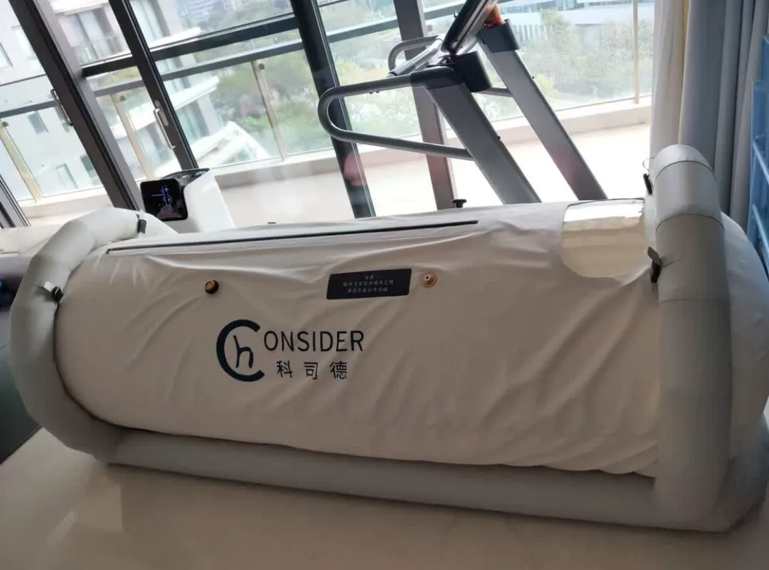 CONSIDER soft hyperbaric chamber installed beside training equipment in a sports recovery studio